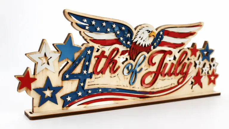 Finished laser-cut patriotic 4th of July decorations made from 3mm basswood, displayed on workshop table with red, white, and blue paint finish
