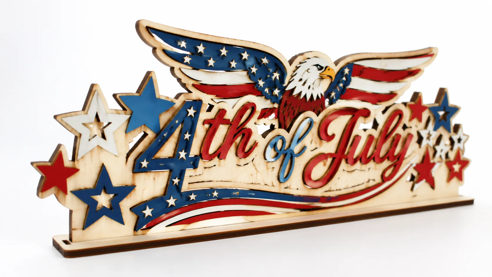 Finished laser-cut patriotic 4th of July decorations made from 3mm basswood, displayed on workshop table with red, white, and blue paint finish