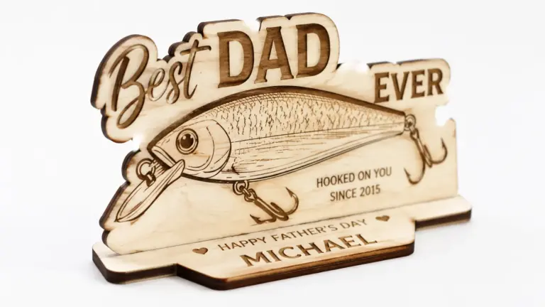 Personalized laser-cut fishing gift plaque made from 3mm basswood, displayed on workshop table with laser engraver in background