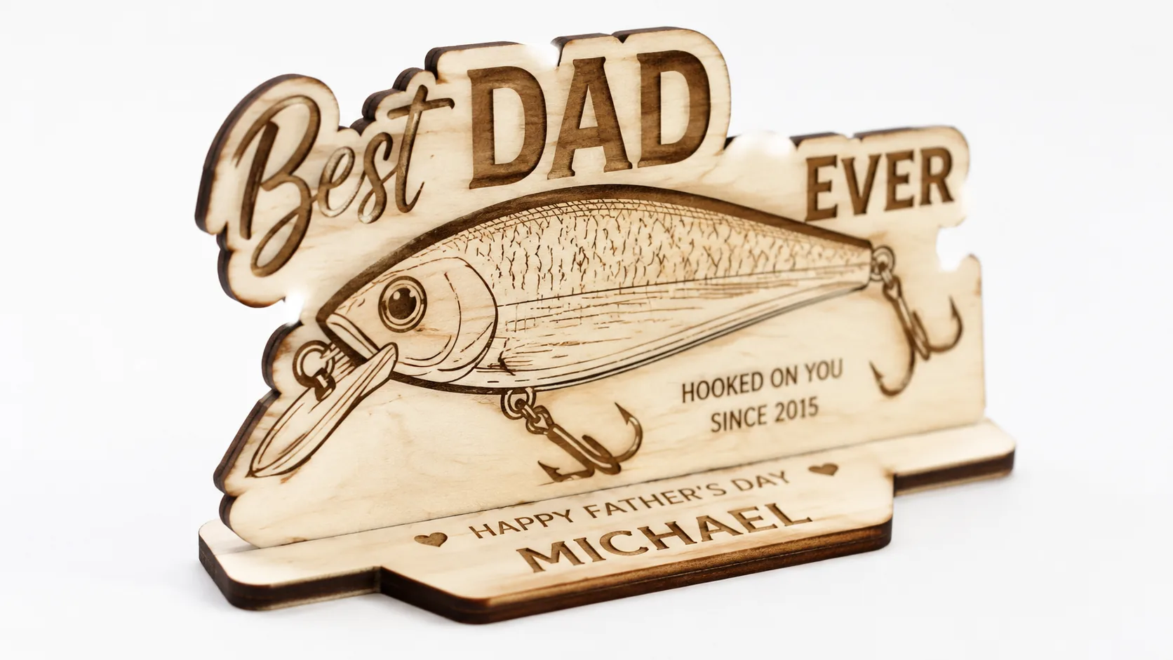 Personalized laser-cut fishing gift plaque made from 3mm basswood, displayed on workshop table with laser engraver in background