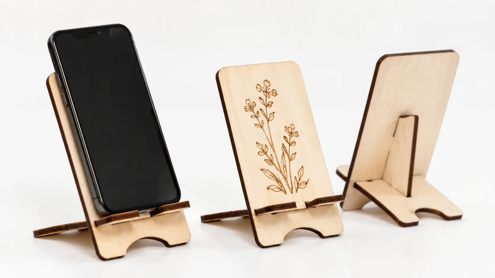 Finished laser cut wooden phone stands made from 3mm basswood, displayed on workshop table with finished edges ready to sell