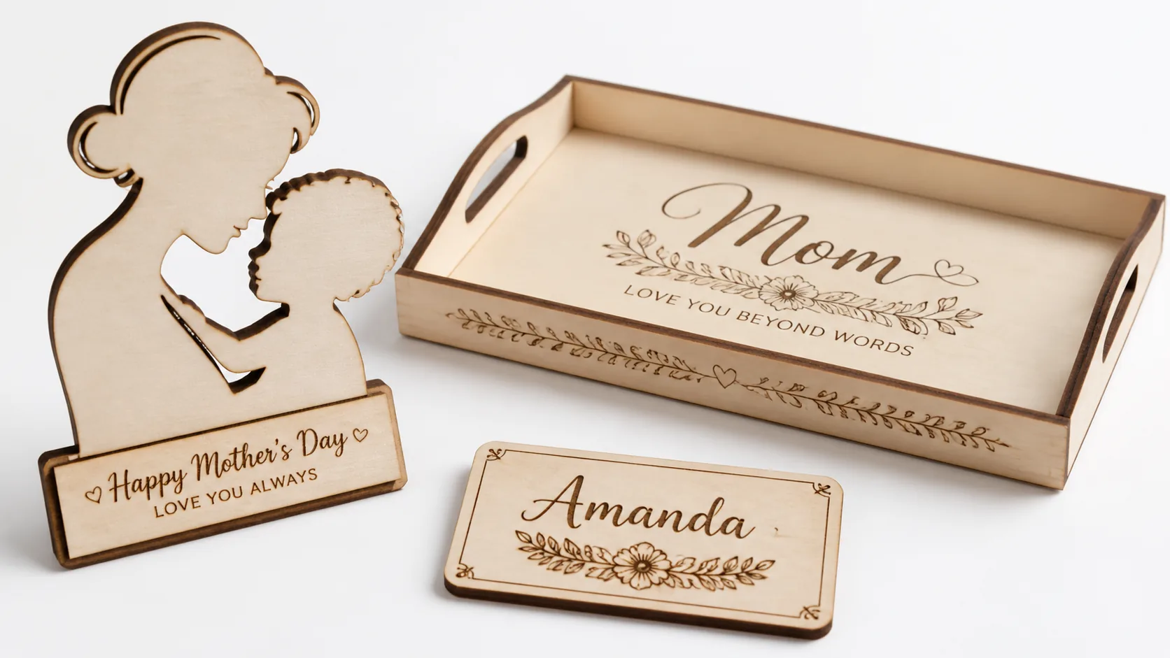 Laser-cut Mother's Day basswood gift items displayed on workshop table, including personalized silhouette art, engraved wooden tray, and name plaques