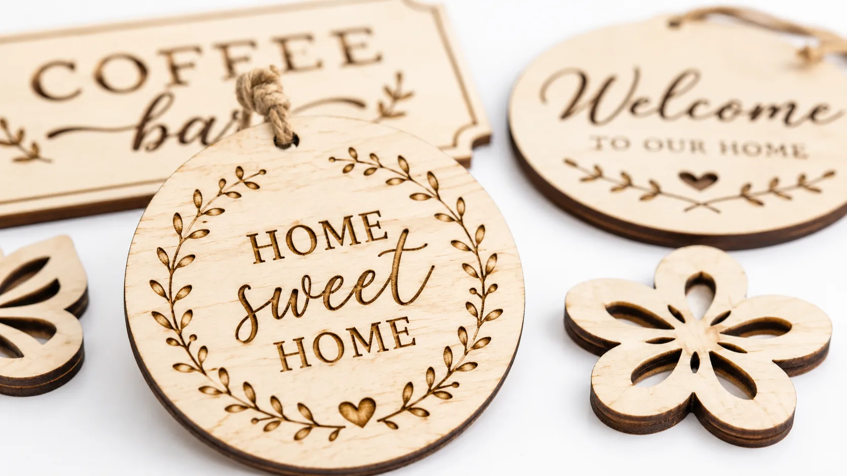Laser-cut basswood signs and ornaments displayed on a clean workshop table, pale cream wood faces with dark brown laser-cut edges